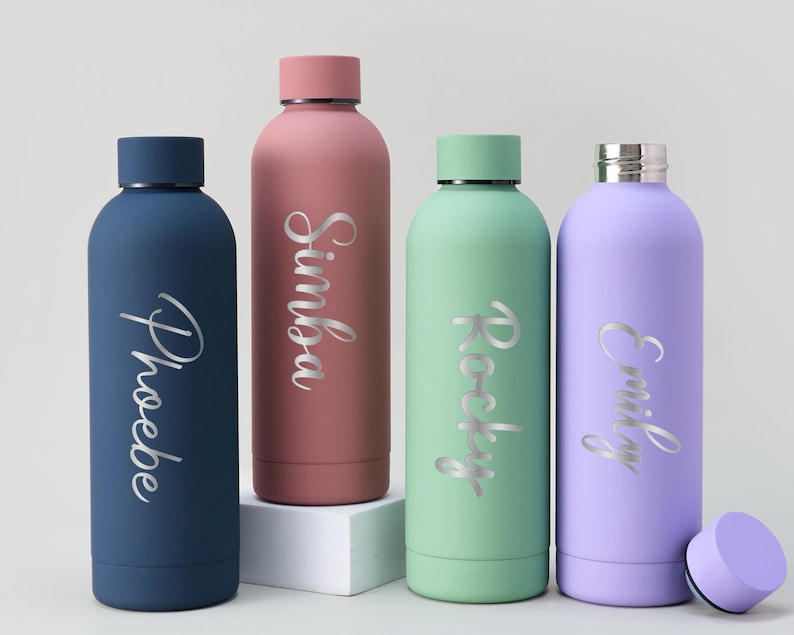 May include: Four insulated water bottles in navy blue, dusty rose, mint green, and lavender. Each bottle has a silver name inscription: Phoebe, Simba, Rocky, and Emily. The bottles have matching colored lids.