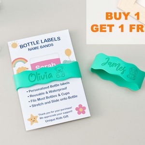 May include: Two teal silicone bottle bands with wavy edges, one wrapped around a white product card labeled BOTTLE LABELS NAME BANDS and the other loose. The bands feature engraved names Olivia and James with small bear and lion icons.