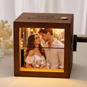 Peut inclure: Un cube photo en bois avec une photo d'un couple, éclairée de l'intérieur. Le cube a une manivelle sur le côté et les mots "Always Remembered" gravés sur le dessus. La photo montre un homme et une femme se regardant.
