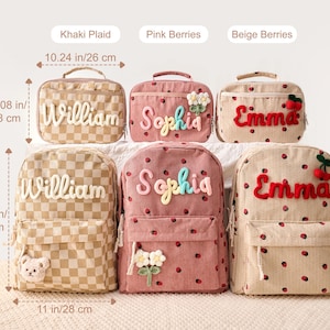 May include: Three lunch bags and three backpacks in Khaki Plaid, Pink Berries, and Beige Berries patterns. Lunch bags measure 10.24 inches by 7.08 inches. Backpacks measure 13.58 inches by 11 inches. Each item features embroidered names and appliques.