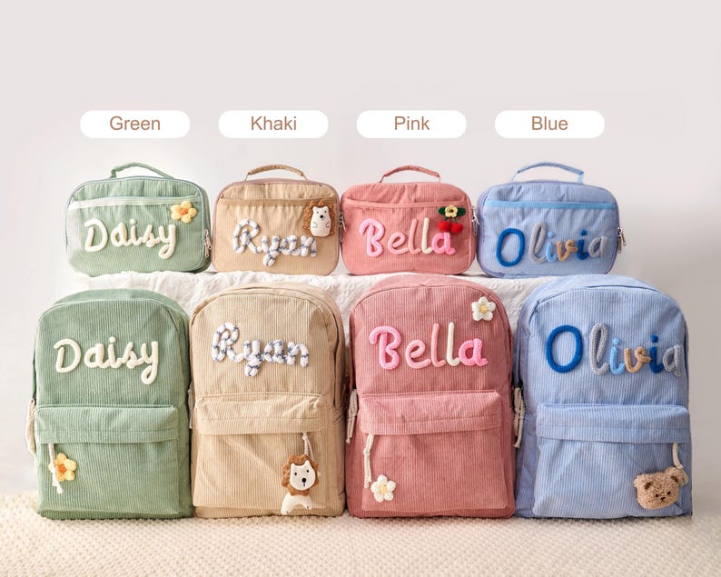 May include: Four corduroy backpacks and four matching lunch bags in green, khaki, pink, and blue. Each item features a personalized name in raised, textured lettering and a small decorative plush accent, such as a flower, lion, or bear.
