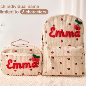 May include: A beige corduroy backpack and matching lunch bag featuring a red strawberry pattern. Both items display the name Emma in red embroidered script with a small red cherry applique. Text above states: Each individual name is limited to 8 characters.