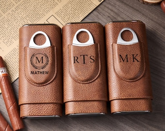 May include: Three brown leather cigar cases with silver cigar cutters. Each case has a pocket with initials or a name engraved. The first case has the initial "M" with the name "MATHEW" below. The other cases have the initials "RTS" and "MK".