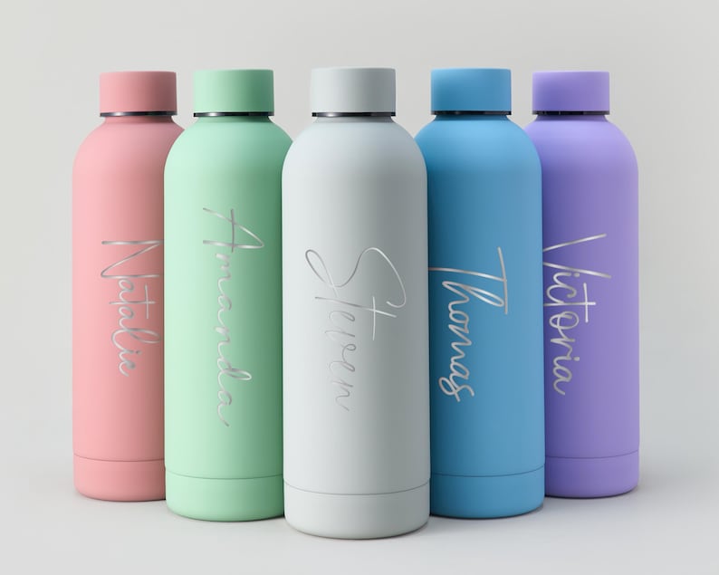 May include: Five colorful insulated water bottles in pink, green, white, blue, and purple. Each bottle has a matching cap and a name in silver script: Natalia, Amanda, Steven, Thomas, and Victoria. The bottles are cylindrical.