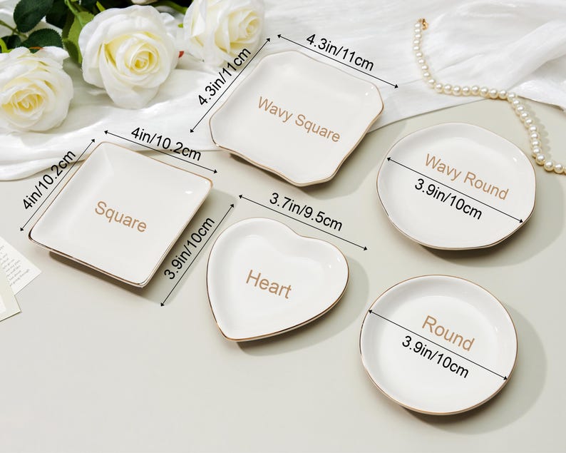 May include: A collection of white ceramic dishes in various shapes: square, wavy square, heart, round, and wavy round. Each dish has a gold rim and the shape name printed in gold. Measurements are provided in inches and centimeters.