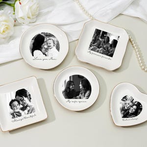 May include: A collection of white ceramic trinket dishes in various shapes: round, square, and heart-shaped. Each dish features a black and white photograph and a gold rim. The dishes are inscribed with phrases like "Love you Mom" and "My forever friends."
