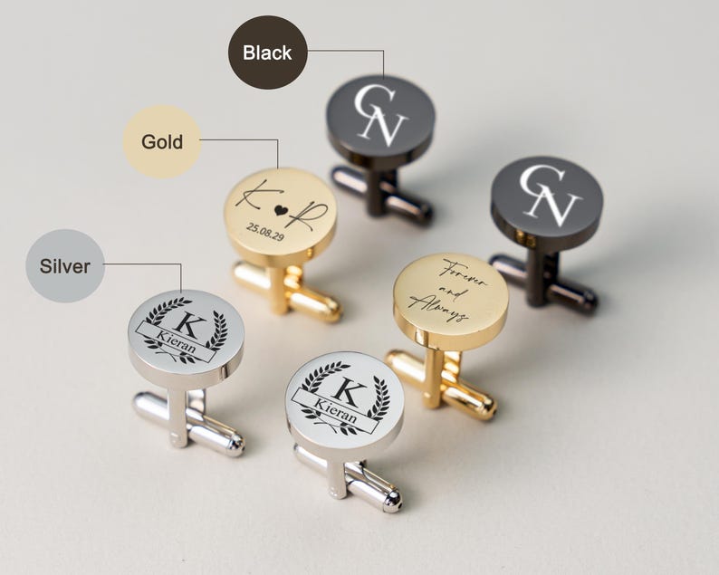 May include: Cufflinks in gold, silver, and black with personalized engravings. The gold cufflinks feature initials and a date, while the silver ones display a name within a laurel wreath. The black cufflinks have initials.