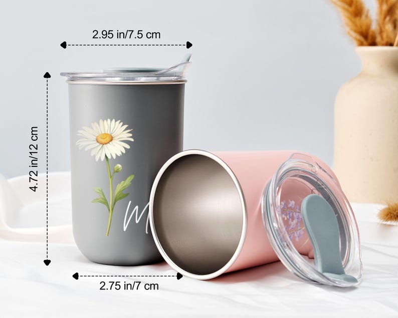 Op de afbeelding: Twee roestvrijstalen reisbekers. E&eacute;n is grijs met een madeliefjesafbeelding en het woord "m" in het wit. De andere is roze, met een doorzichtig deksel. De grijze beker is 12 cm hoog en heeft een diameter van 7 cm. De roze beker heeft een diameter van 7,5 cm.