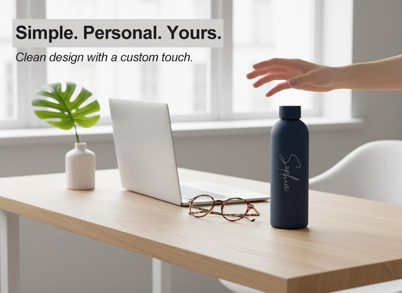 May include: A navy blue water bottle with the name "Sophia" in cursive script. The bottle sits on a light wood desk with a laptop, eyeglasses, and a small vase with a green leaf. Text above reads "Simple. Personal. Yours."