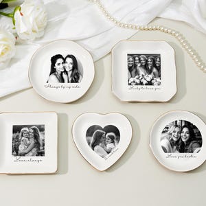May include: A collection of white ceramic trinket dishes with gold rims, each featuring a black and white photograph. The dishes are in various shapes, including round, square, and heart-shaped, with phrases like "Always by my side" and "Love always" printed on them.