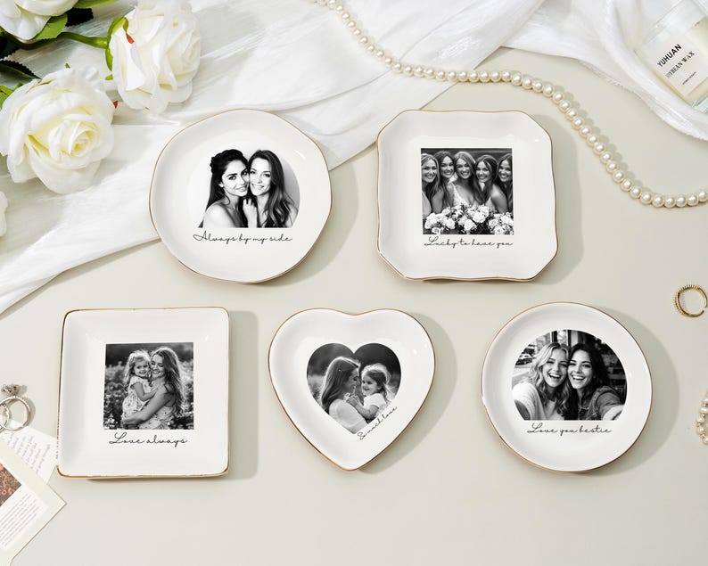 May include: A collection of white ceramic trinket dishes with gold rims, each featuring a black and white photograph. The dishes are in various shapes, including round, square, and heart-shaped, with phrases like "Always by my side" and "Love always" printed on them.