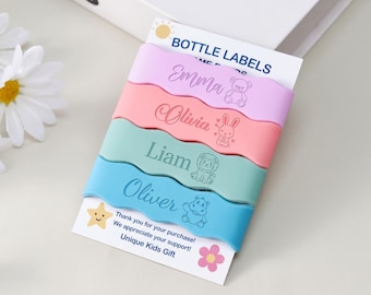 May include: Four wavy silicone bottle labels in pastel purple, pink, mint green, and blue. Each label features a name and a small animal illustration: Emma with a bear, Olivia with a rabbit, Liam with a lion, and Oliver with a hippo. The labels are attached to a white card with the text BOTTLE LABELS.