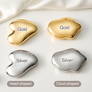 May include: Four metallic facial massage tools, two gold and two silver. The gold tools are heart-shaped and cloud-shaped. The silver tools are also heart-shaped and cloud-shaped. Each tool has the color name printed on it.