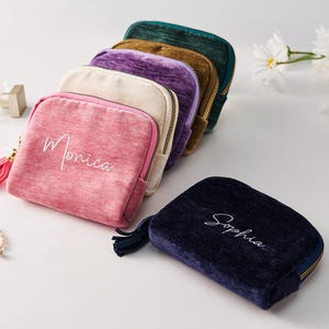 May include: A collection of five velvet zippered pouches in pink, cream, purple, brown, and dark green, with a separate dark blue pouch. The pink pouch features the name Monica, and the dark blue pouch features the name Sophia in white script.