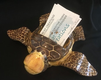 May include: A ceramic turtle-shaped business card holder. The turtle is brown and tan with a glossy finish. The business card holder is filled with white business cards. The text on the business cards reads "BOBCAT CREATIONS" and "EGINA FORSYTHE-TOBIN OWNER/DESIGNER".