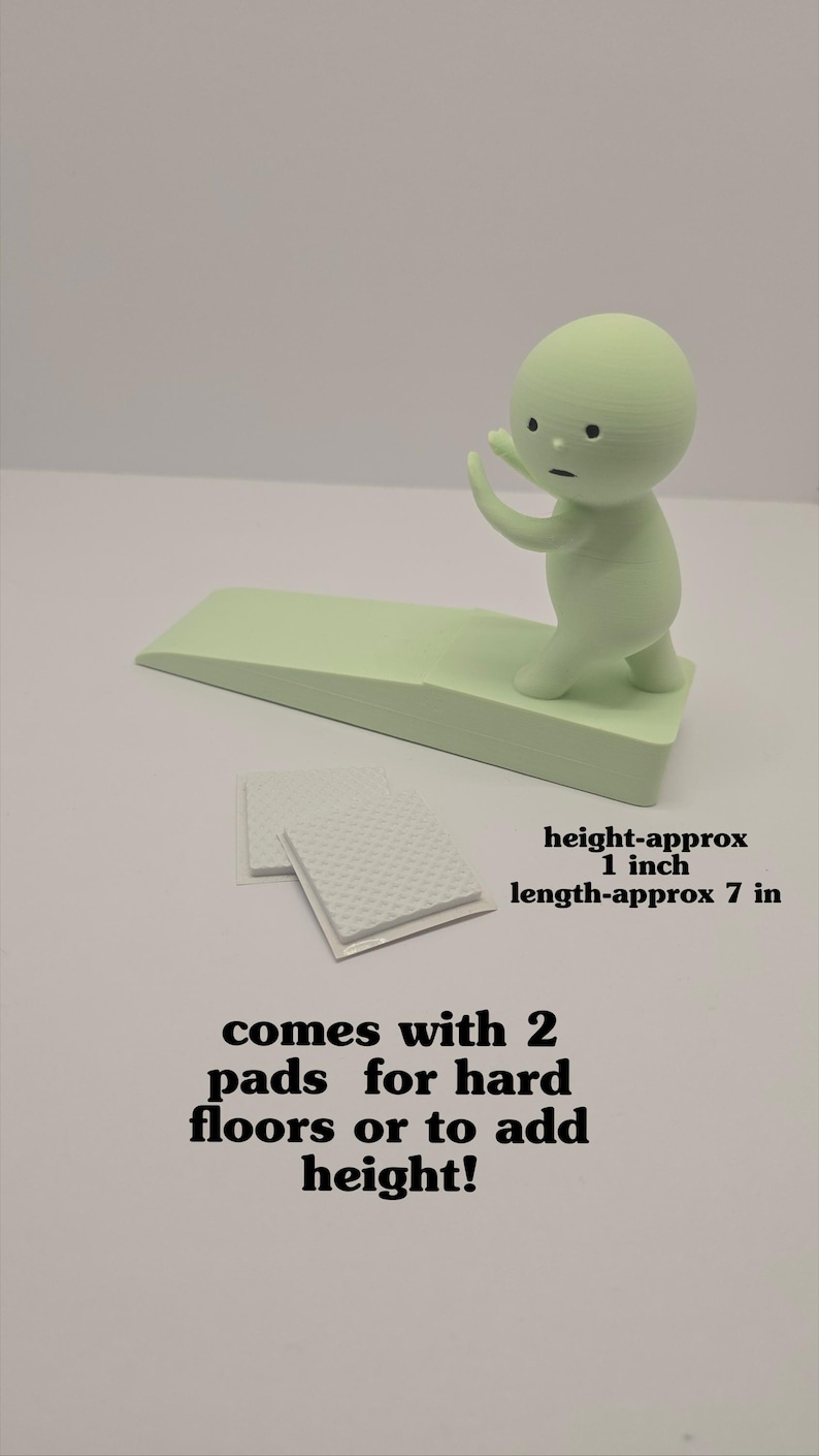 May include: A light green door stop with a small figure on top, approximately 1 inch high and 7 inches long. Includes two pads for hard floors or to add height.