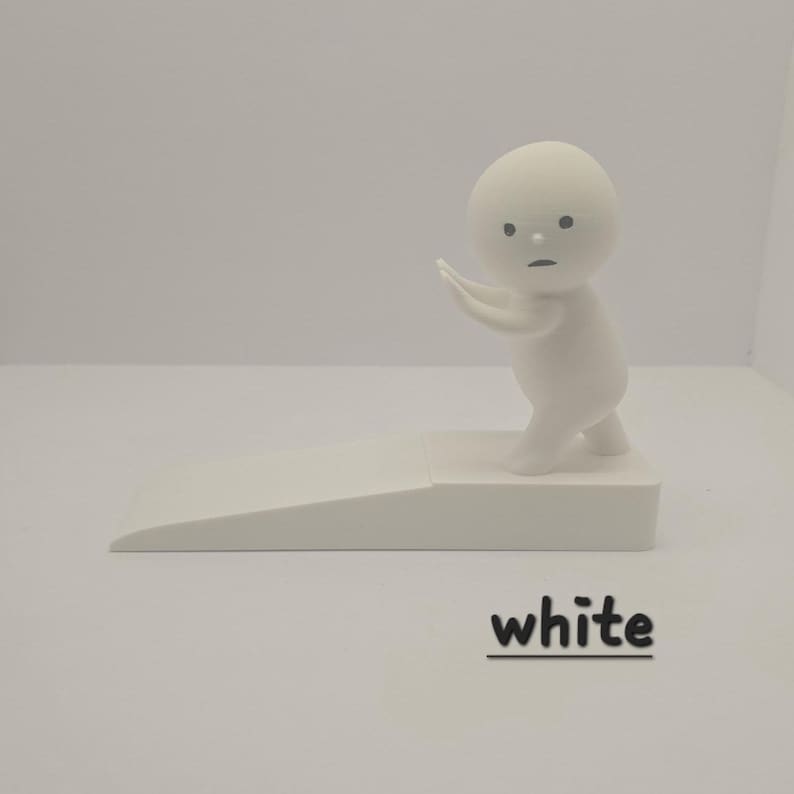 May include: A white figurine of a small person with a round head and outstretched arms, standing on a white platform. The figurine is next to a white doorstop with the word "white" in black text.