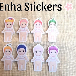 May include: A collection of eight die-cut stickers featuring cartoon-style figures with fruit-themed headwear. The stickers have a white border and the text "Enha Stickers" is at the top.