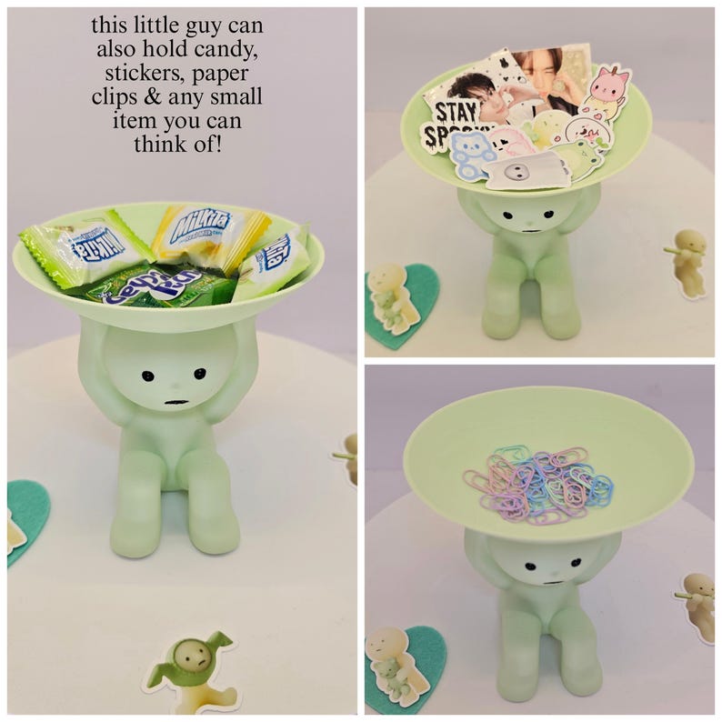 May include: A light green figurine holding a round tray. The tray is filled with candy, stickers, and paper clips. The figurine has a minimalist design and is sitting down. Text on the image says, "this little guy can also hold candy, stickers, paper clips & any small item you can think of!"