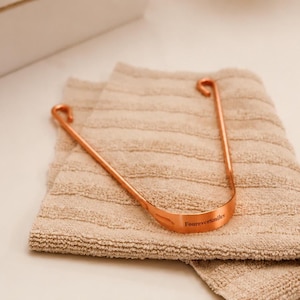 Copper tongue scraper placed on a soft neutral towel with warm lighting, showcasing a minimal eco-friendly oral care routine aesthetic.