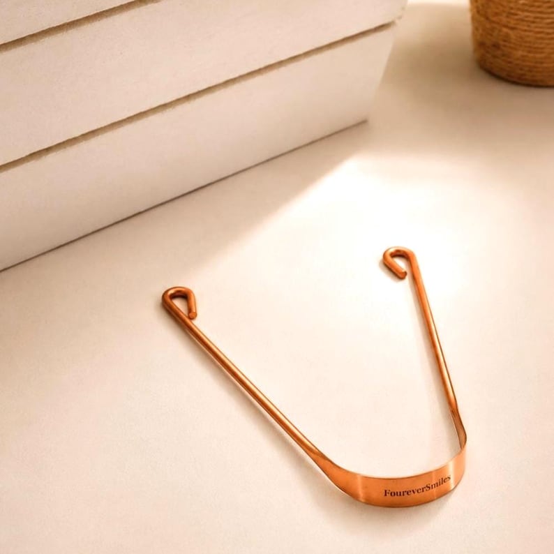 Copper tongue scraper resting on a bright bathroom countertop with soft natural light and warm shadows.
