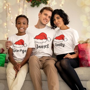 サンタ帽子付きパーソナライズ名前入りクリスマスファミリーシャツ、カスタムメリークリスマスマッチングTシャツ、写真用クリスマスパジャマシャツ、