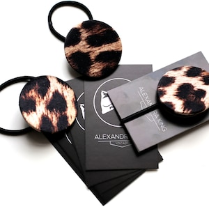 May include: Three black hair ties with leopard print fabric covers. The hair ties are on a black card with the text "Alexandra King Vintage" printed in white.