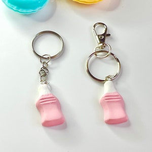May include: Two pink and white bottle-shaped keychains with silver key rings and chains. The keychains are on a white background.