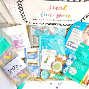 May include: A gift box filled with self-care items. Includes a pair of gray socks with donut designs, face masks, foot pack, lip balm, tea bags, and a four-leaf clover charm. The box lid reads "just for you, special moments, special boxes."