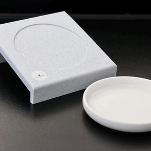 Könnte beinhalten: Eine weiße Keramik-Futternapf und eine graue, strukturierte, erhöhte Plattform für Futternapf.