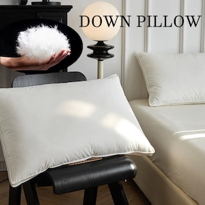Könnte beinhalten: Weißes Daunenkissen auf einem schwarzen Stuhl mit dem Text "DOWN PILLOW". Eine Nahaufnahme zeigt flauschige Daunenfedern. Ein weiteres weißes Kissen liegt auf einem Bett mit weißem Laken. Die Szene ist gut beleuchtet.