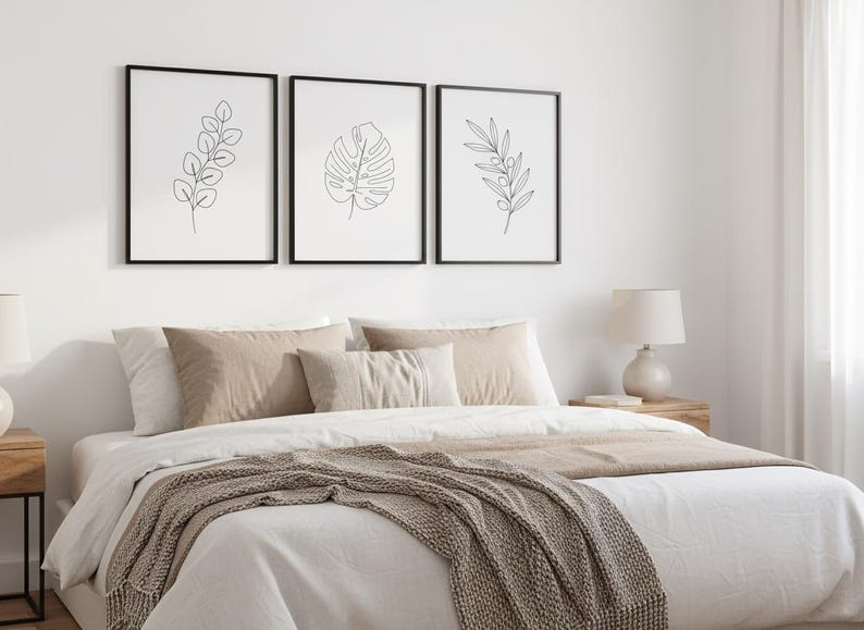 Puede incluir: Tres estampados bot&aacute;nicos enmarcados con marcos negros cuelgan sobre una cama. Los estampados presentan dibujos lineales minimalistas de hojas. La cama est&aacute; hecha con s&aacute;banas blancas, almohadas beige y una manta marr&oacute;n. Una l&aacute;mpara de noche se encuentra en una mesita de noche de madera.