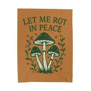 以下が含まれることがあります： 緑色の「LET ME ROT IN PEACE」の文字が入った、オレンジ色のブランケット。白い茎と緑のつる、星に囲まれた、3つの緑色のキノコのグラフィックが特徴です。