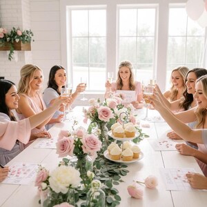 May include: A group of women celebrating at a table decorated with pink roses, greenery, and cupcakes. They are toasting with champagne flutes in a bright, airy room. Balloons are visible in the background. The scene suggests a bridal shower or similar event.