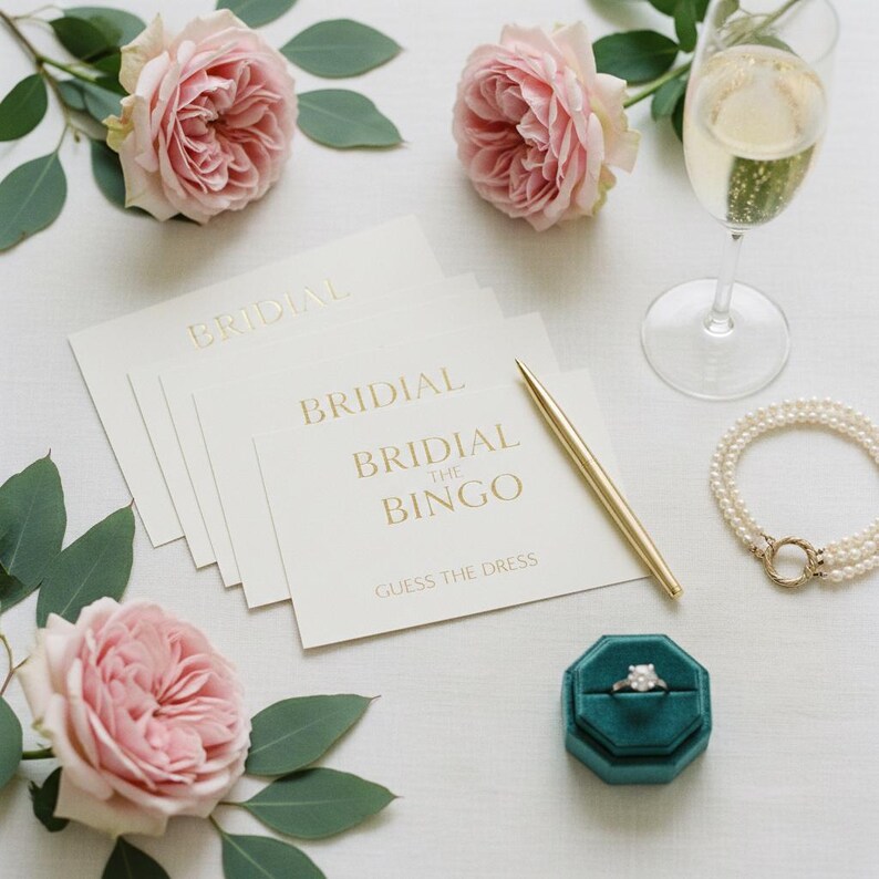 May include: A bridal shower scene with cards that read "Bridal Bingo" and "Guess the Dress". The scene includes pink roses, a champagne flute, a pearl bracelet, a gold pen, and a ring in a teal velvet box.