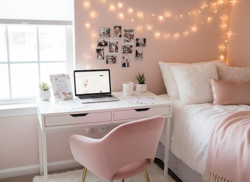May include: A cozy bedroom scene with a white desk, a pink velvet chair, and a laptop. A bed with white bedding and pink pillows is in the background. String lights and framed photos decorate the pink walls. A small succulent plant sits on the desk.