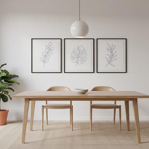Puede incluir: Una mesa de comedor de madera clara con dos sillas y un cuenco peque&ntilde;o. Tres grabados bot&aacute;nicos enmarcados cuelgan de la pared blanca de arriba. Una planta en maceta est&aacute; en la esquina. Una l&aacute;mpara colgante blanca cuelga sobre la mesa.