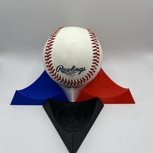 May include: A baseball display stand with a white baseball with red stitching and the Rawlings logo. The stand is made of three pieces: a blue, a red, and a black triangular piece.