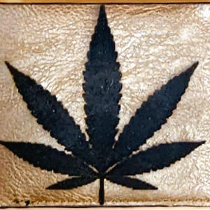 May include: A brown leather wallet with a black marijuana leaf design.