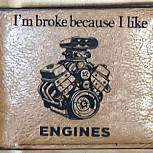 May include: A rectangular plaque with the text "I'm broke because I like ENGINES." The plaque features a detailed black and white illustration of an engine. The background has a textured, metallic appearance.