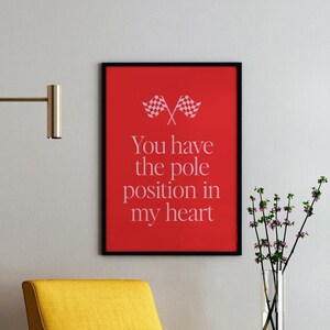 Puede incluir: Un sillón amarillo con patas negras en una sala de estar con una pared blanca y un póster rojo enmarcado con el texto "You have the pole position in my heart" y un gráfico de bandera a cuadros.