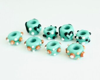 Peut inclure: Huit perles en verre turquoise avec différents motifs. Certaines perles ont des pois blancs et noirs, d'autres ont des pois bruns et blancs, et l'une a un cœur noir.