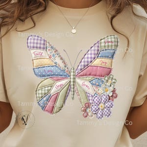 Op de afbeelding: Beige T-shirt met een kleurrijk patchwork vlinderontwerp. De vlindervleugels zijn gemaakt van verschillende stoffen met patronen en bevatten woorden als "Geloof" en "Vrede". Het ontwerp bevat bloemmotieven.