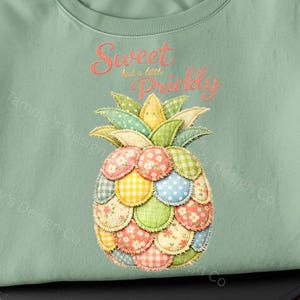 May include: A pale green sweatshirt with a patchwork pineapple design. The pineapple is made of various patterned fabrics in pink, yellow, green, and blue. The text "Sweet but a little Prickly" is embroidered above the pineapple.