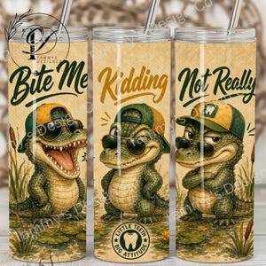 May include: A cylindrical tumbler with a metal straw featuring a beige background and three illustrations of a cartoon alligator wearing sunglasses and a baseball cap. The text reads Bite Me, Kidding, and Not Really, with a tooth icon and the text Little Teeth Big Attitude.