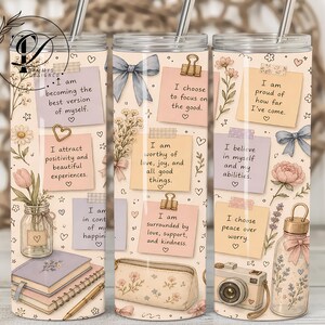 May include: Three cylindrical tumblers with metal straws featuring a cream background decorated with pastel sticky notes containing positive affirmations, floral illustrations, blue bows, a camera, a pencil, a notebook, and a pencil case.