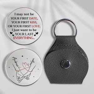 May include: A silver-colored keychain with a black leather holder and two round metal tokens. One token has the text "I may not be your first date..." and the other has the names "Andrew" and "Evelyn" with a heart design.