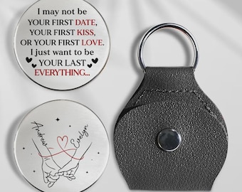 May include: A silver-colored keychain with a black leather holder and two round metal tokens. One token has the text "I may not be your first date..." and the other has the names "Andrew" and "Evelyn" with a heart design.