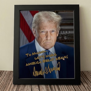 May include: A framed photograph of a man in a suit with a handwritten message that says "To Michael, Let's Make America Great Again!" and a signature that says "Donald Trump".
