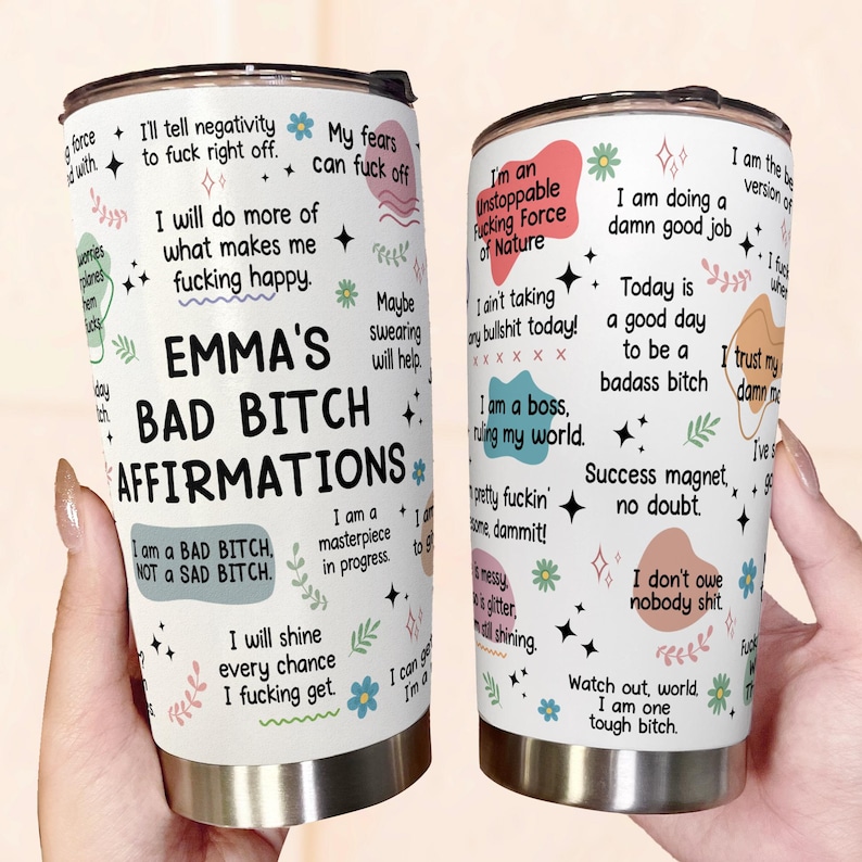 May include: A white stainless steel tumbler with a black lid, featuring the text "EMMA'S BAD BITCH AFFIRMATIONS" and various affirmations in a playful font. The tumbler is decorated with floral and star graphics.